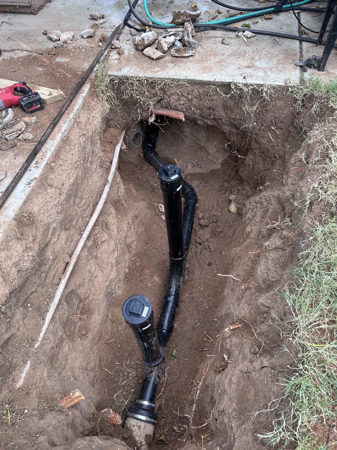 Exposed sewer piping with two capped cleanout risers in an excavated trench