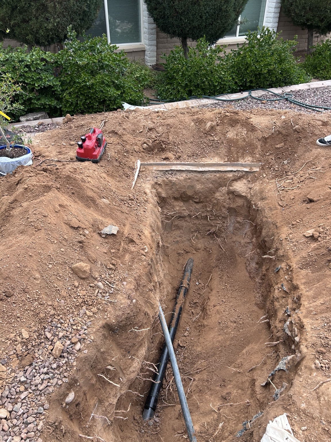 Wide view of an excavated sewer work area beside a home